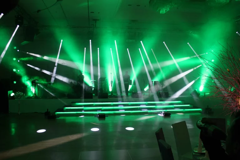 Eine Showtreppe, dahinter eine Bühne. Moving-Heads wirbeln wild durch die Gegend, alles in grün-weisses Licht getaucht.