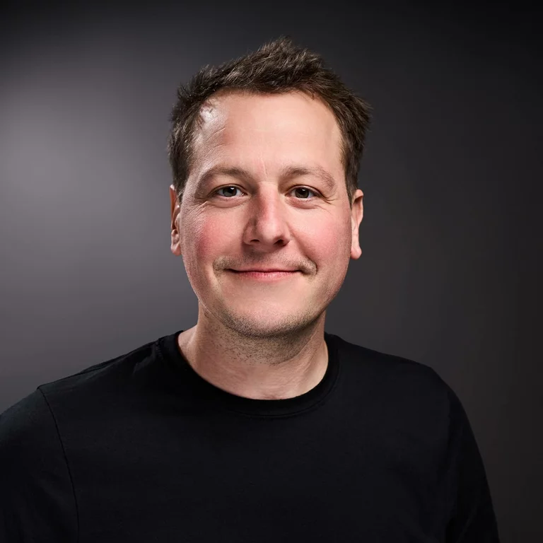 Portrait-Foto von Florian Grund, Geschäftsführer, in einem schwarzen Pullover. Er lächelt.