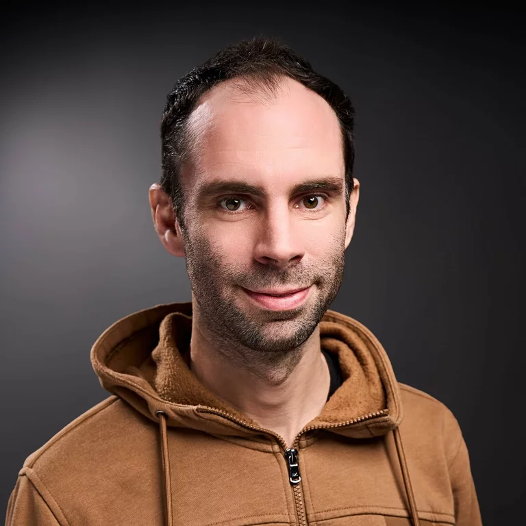 Portrait-Foto von Oliver Klostermann, Projektleitung, in einem braunen Kapuzenpullover. Er lächelt.