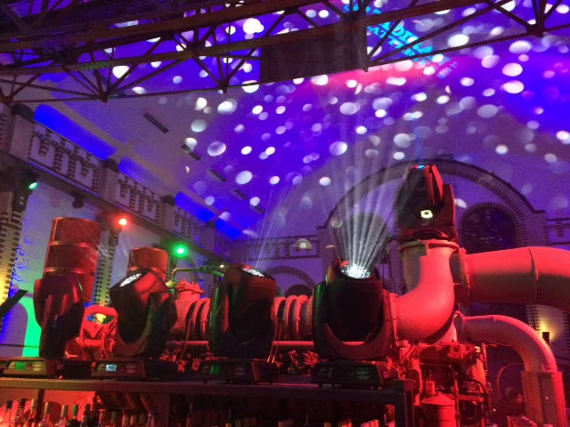 Das Bild zeigt eine der großen alten Pumpenmaschinen aus dem Wasserwerk. die Maschine ist rot beleuchtet, dahinter sieht man das alte Gemäuer und die Hallendecke, die blau mit weissen Punkten beleuchtet sind. Oben links sieht man Teile einer alten Industrie-Brücke aus Stahlträgern.Alles sieht sehr festlich aus.